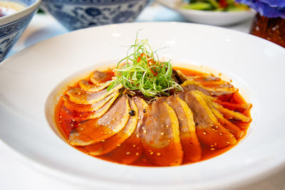Slices of tender duck in a spicy chili oil sauce, topped with spring onions and sesame, from Mo Jasmine Zurich.