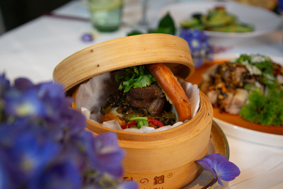 Golden Gua Bao with succulent braised pork belly and pickled vegetables, served in a traditional bamboo steamer at Mo Jasmine Zurich.